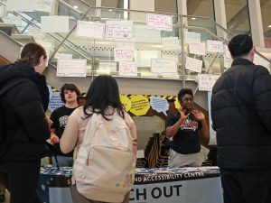 Two students stand behind a table and speak to fellow students about the services and resources available at Brock University's Student Wellness and Accessibility Centre.