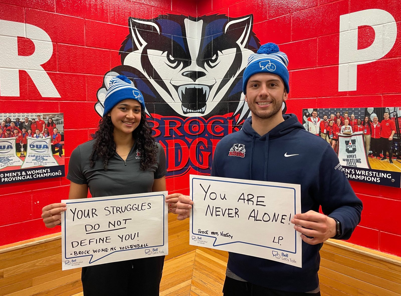 A woman and a man stand indoors holding signs with words of positive encouragement regarding mental health.