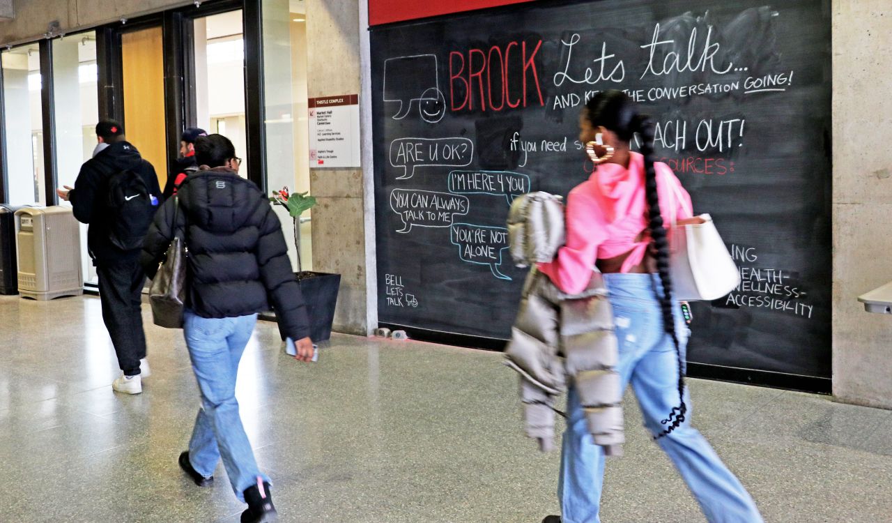 Several students walk by a large chalk board that features mental health resources