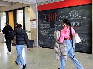 Several students walk by a large chalk board that features mental health resources