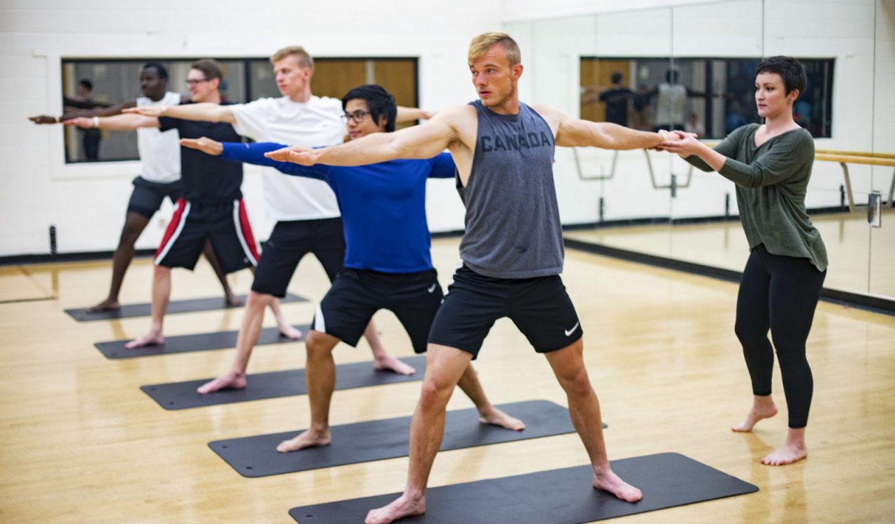 A row of students stands in a yoga pose.
