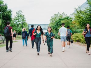 Students walk down a large concrete walkway lined by trees.