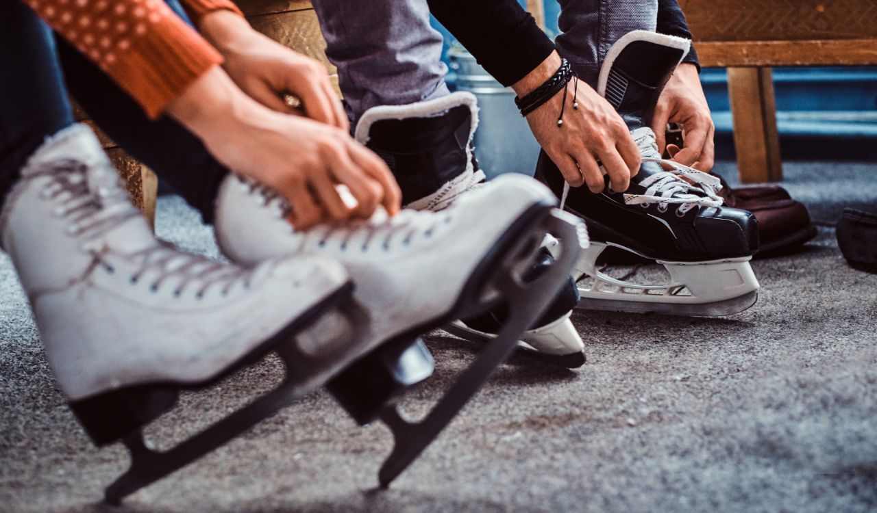 Two people are shown lacing up skates, only their hands and feet visible.