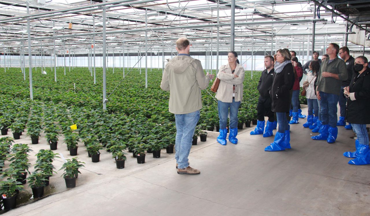 A man speaks to a group of people inside a greenhouse.