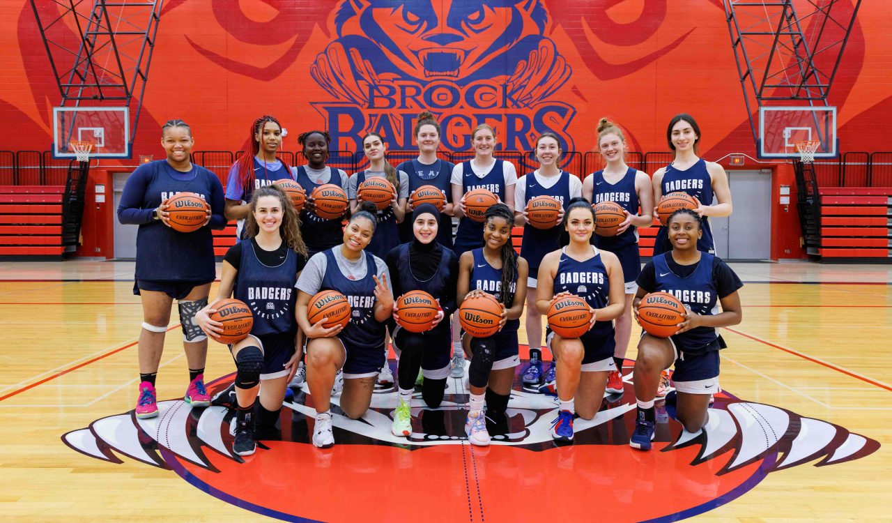 A women’s basketball team stands at centre court in a gymnasium.