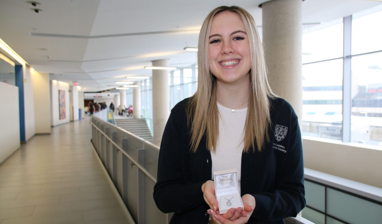 A woman stands in a hallway holding a piece of jewelry in a box.