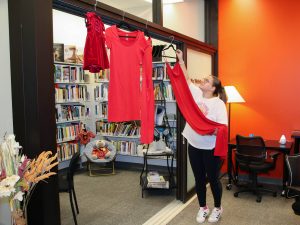 A woman hangs four red dresses over the entrance to a small indoor library.