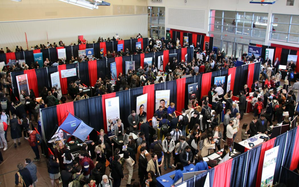 A gymnasium filled with people visiting a variety of booths set up around the room.