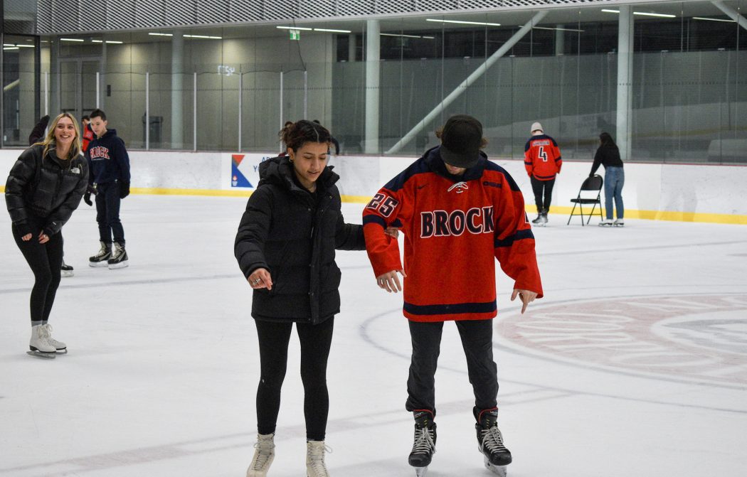 A woman holds onto a man's arm while they both skate in an indoor hockey arena.