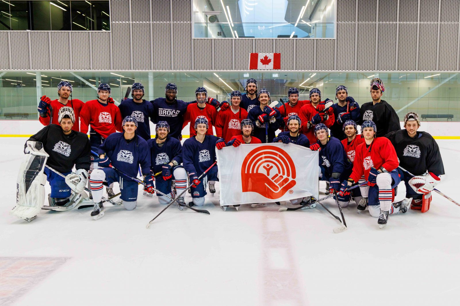 The Brock University Badgers men’s hockey team poses on a sheet of ice holding the United Way flag.