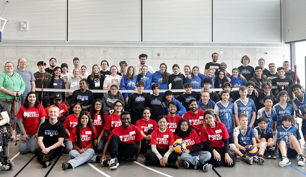 Participants in the Brock Niagara Penguins' Sitting Volleyball Tournament and Brock student volunteers pose for a photo on the volleyball court during a recent tournament