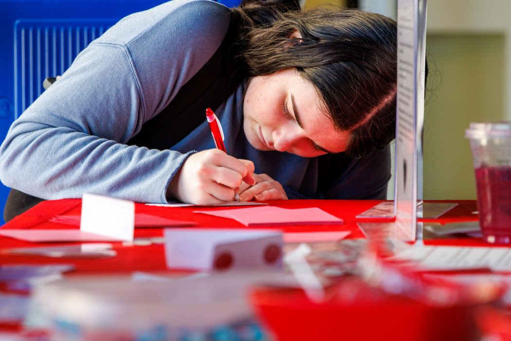 A woman writes a letter on a table using a pen.