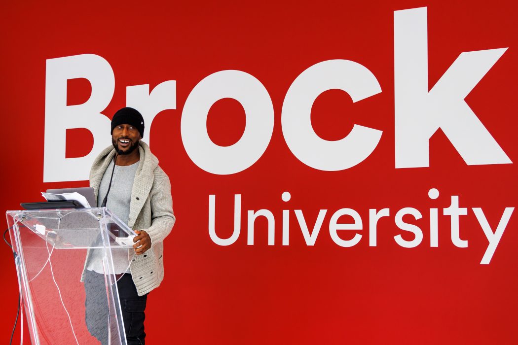 A man stands at a podium in front of a large Brock University sign.