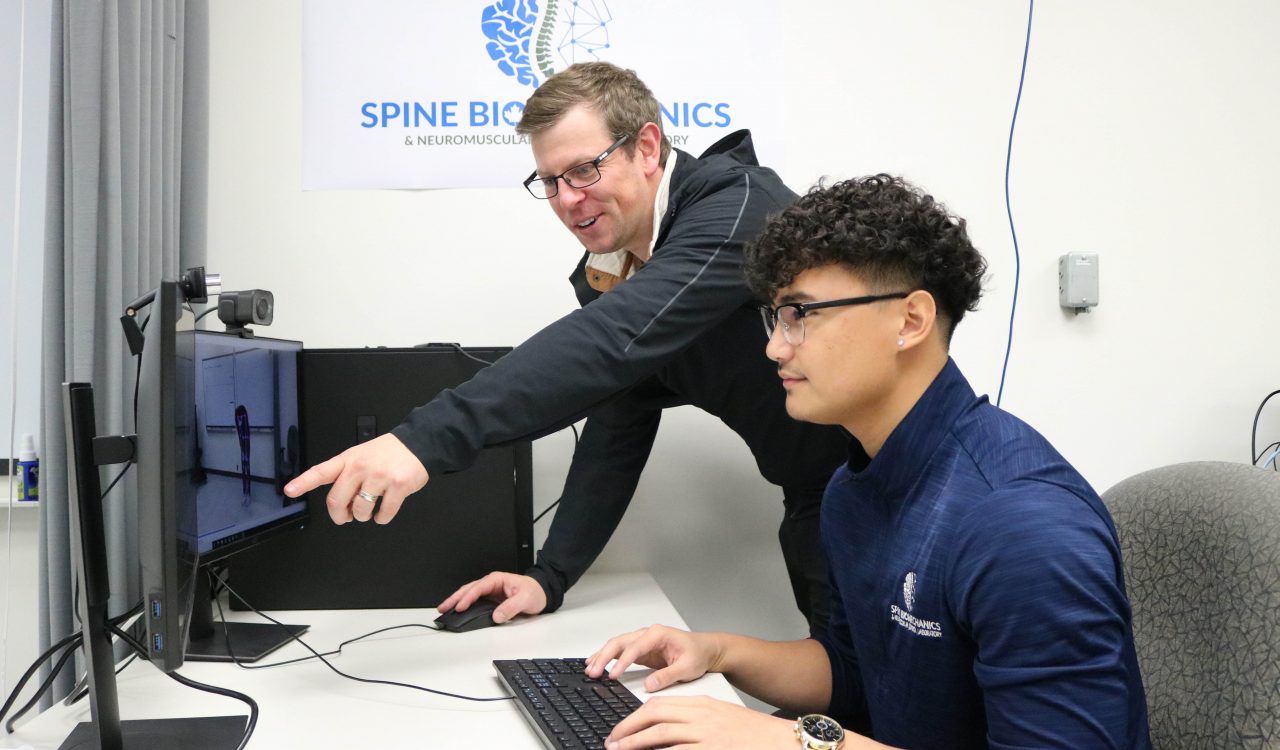 Brock graduate student Carl Alano sits in front of a computer while his thesis supervisor, Assistant Professor of Kinesiology Shawn Beaudette, points to a screen as they review video data.
