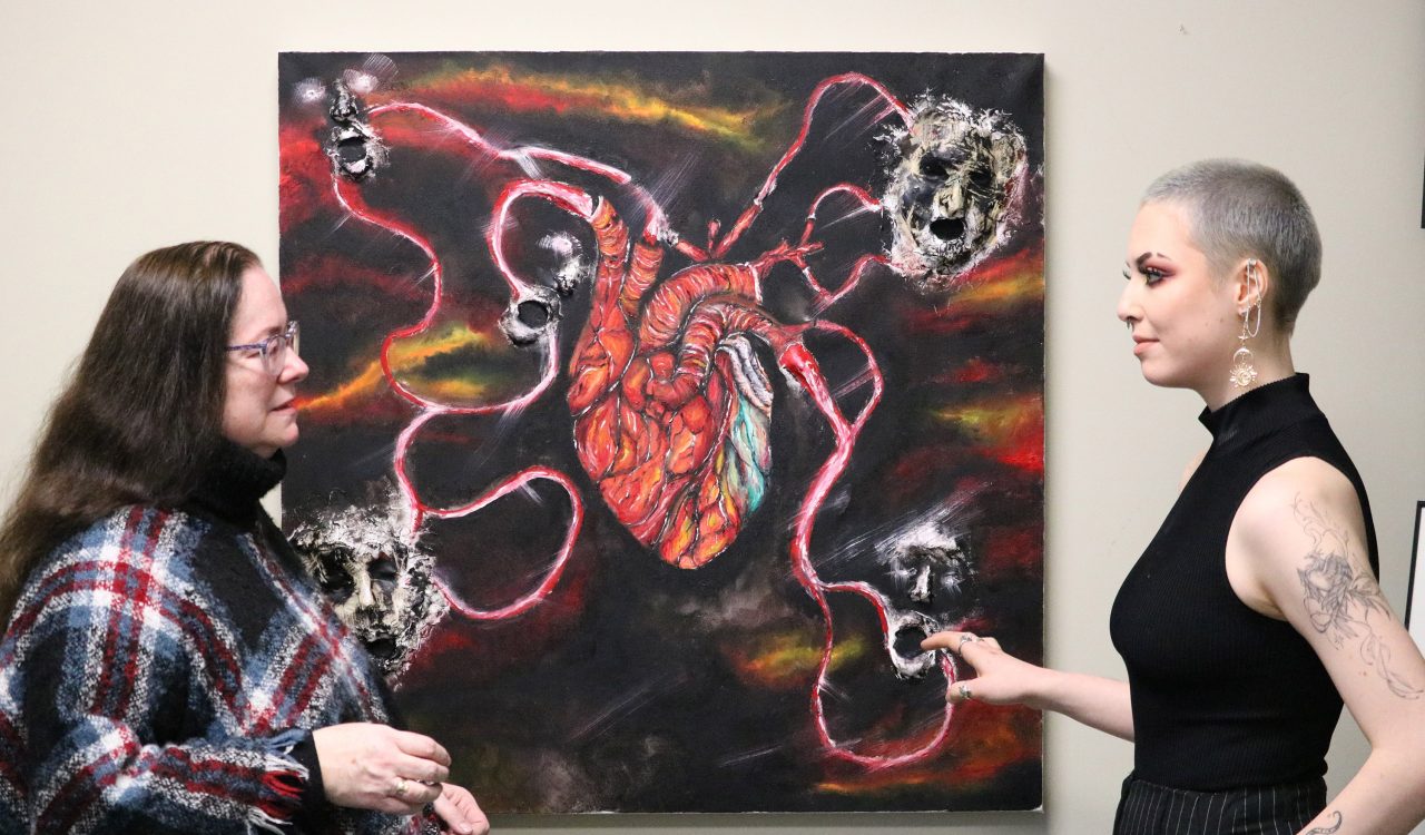 Brock researcher Sheila O’Keefe-McCarthy (left) discusses a mixed-media oil painting of an anatomical heart with 3D faces at the end of four different pictorial representations of veins and arteries extending from the heart with the artist and second-year Brock Nursing student Hannah Michaelson.
