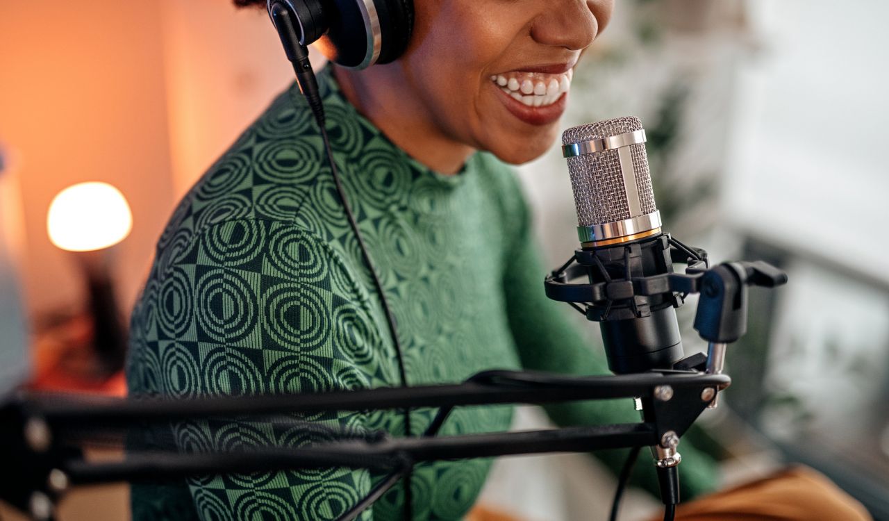 A woman smiles while she speaks into a large microphone used for podcasting.