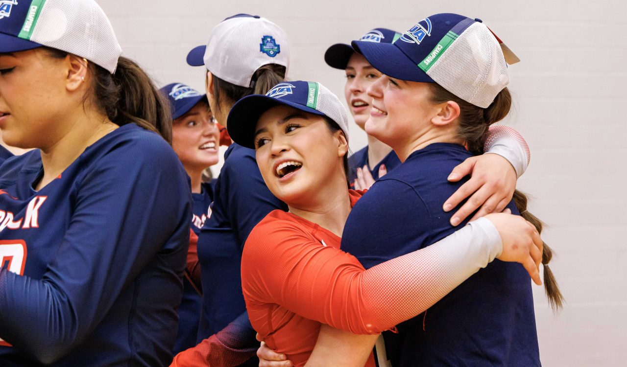 A woman hugs her volleyball teammates following a victory.