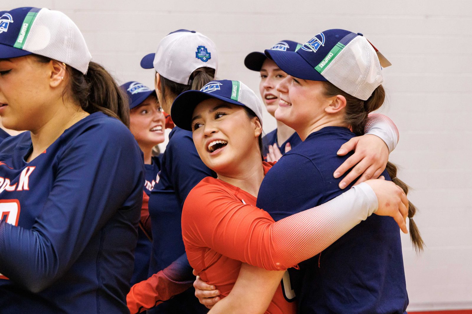 A woman hugs her volleyball teammates following a victory.