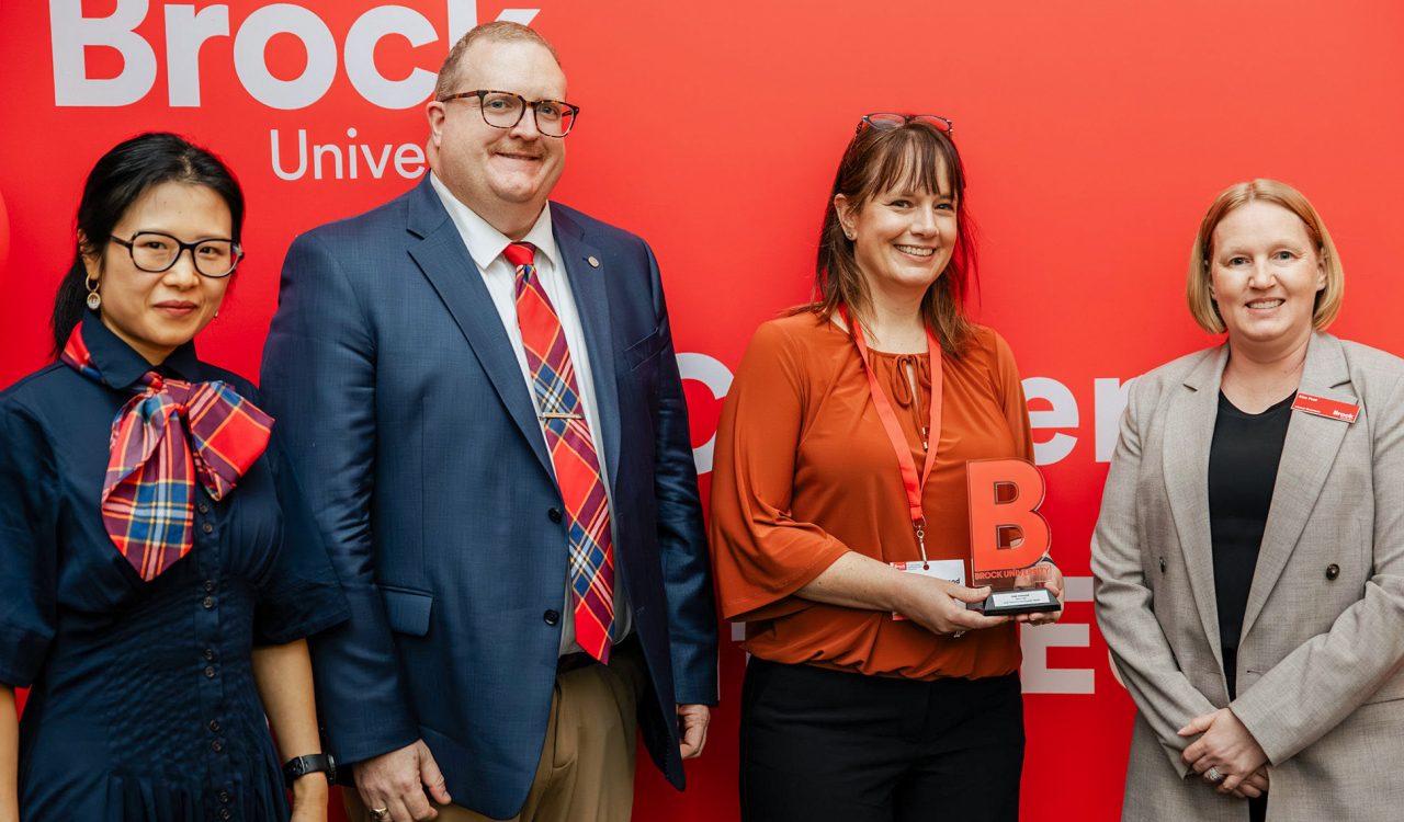 Four people pose in front of a red backdrop with one person holding an award.