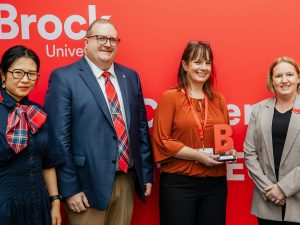 Four people pose in front of a red backdrop with one person holding an award.