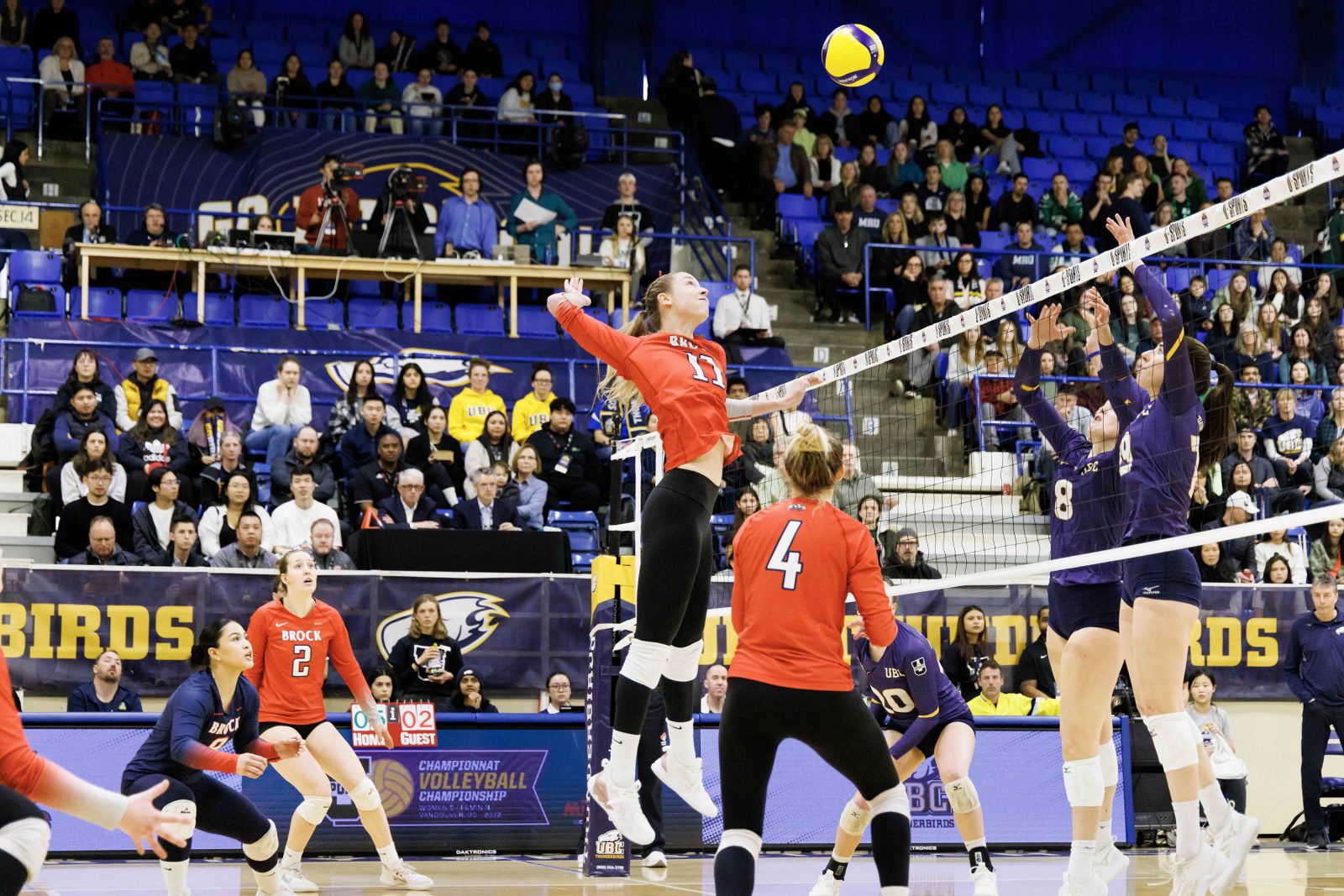 A woman jumps to strike a volleyball indoors.