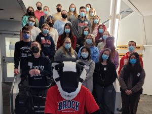 several students in medical masks pose on a staircase while Boomer the Badger kneels in front of them.
