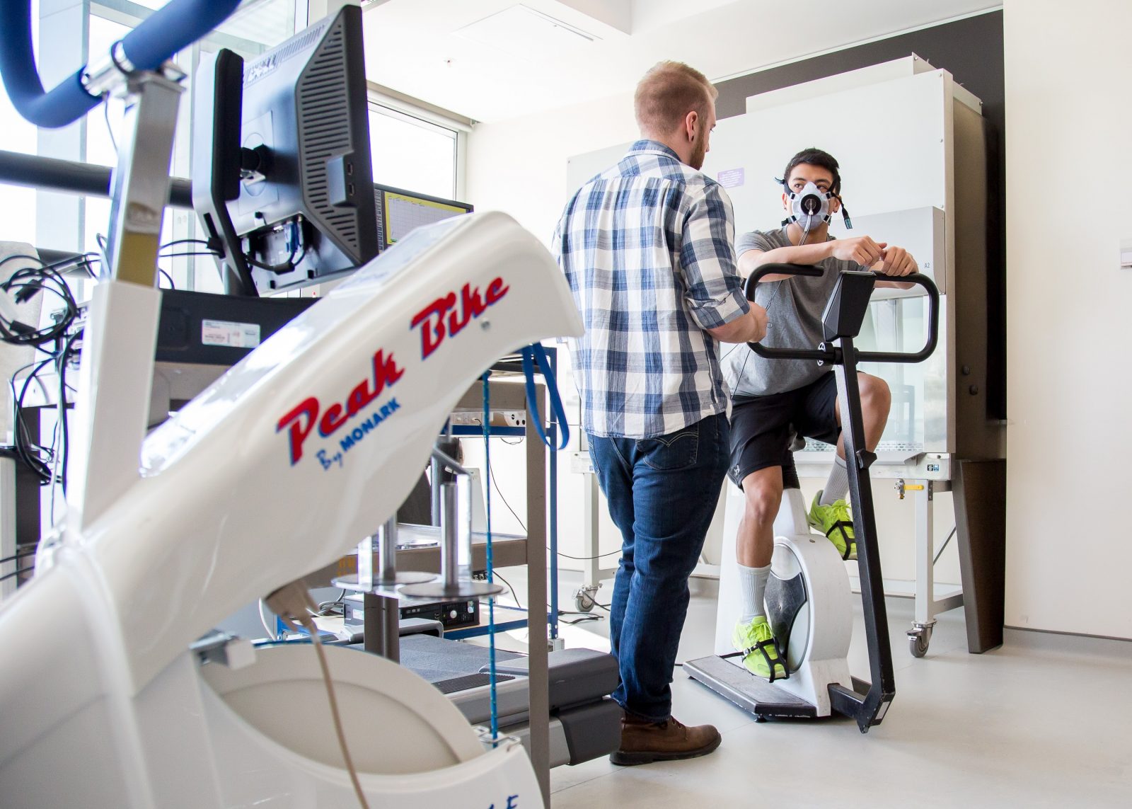 A man collects research data from another man sitting on a stationary bike.