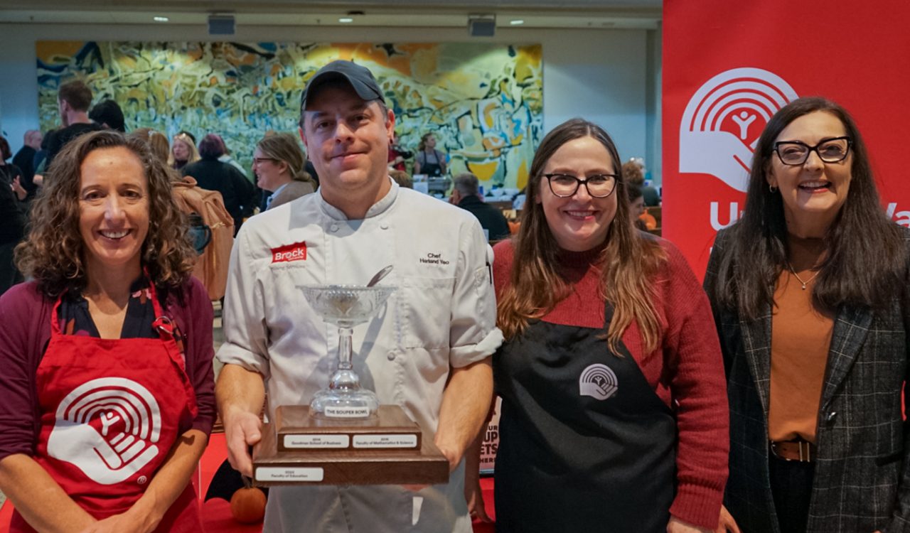 Four people pose with a trophy in a busy cafeteria.