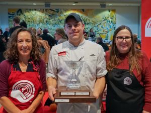 Four people pose with a trophy in a busy cafeteria.
