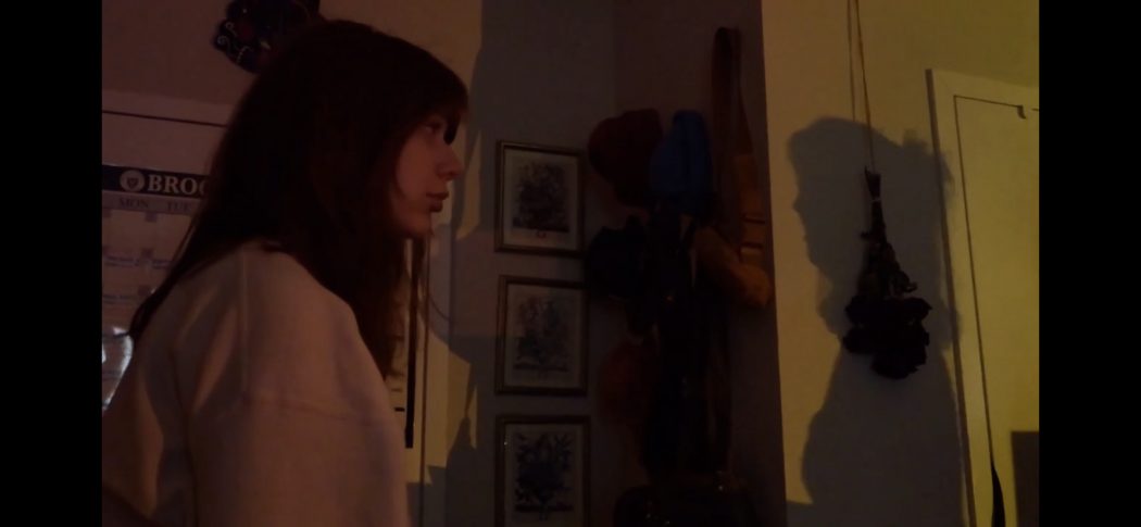 A young woman stares at a shadow in a darkened room