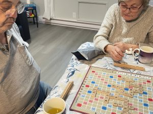 Two elderly people play a game of scrabble while drinking coffee.