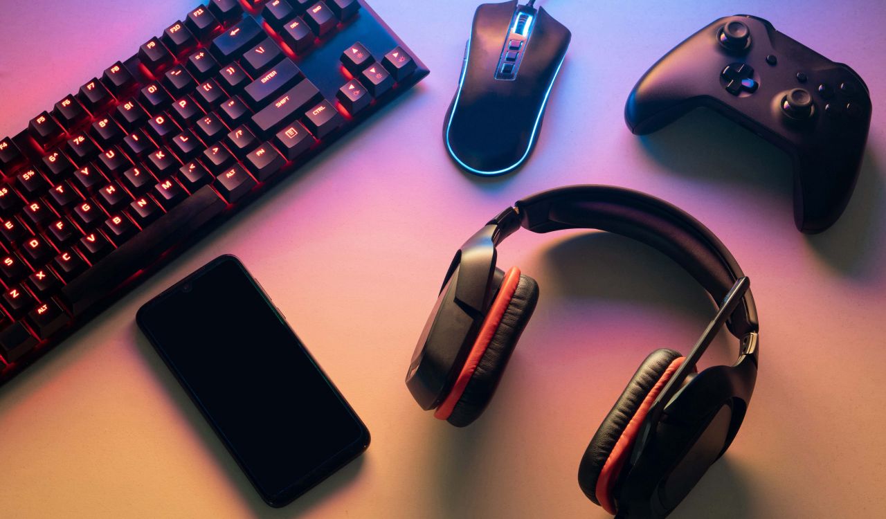top view of a gaming gear, keyboard, mouse, gamepad, joystick, headset and a smartphone on a colorful desk.