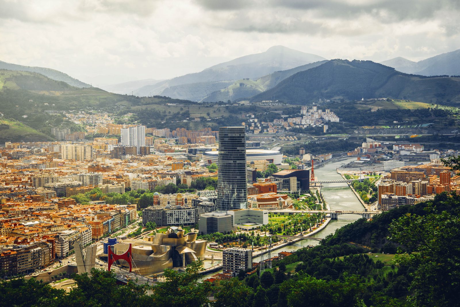 Landscape image of Bilboa, Spain, with buildings and landscape in the background.