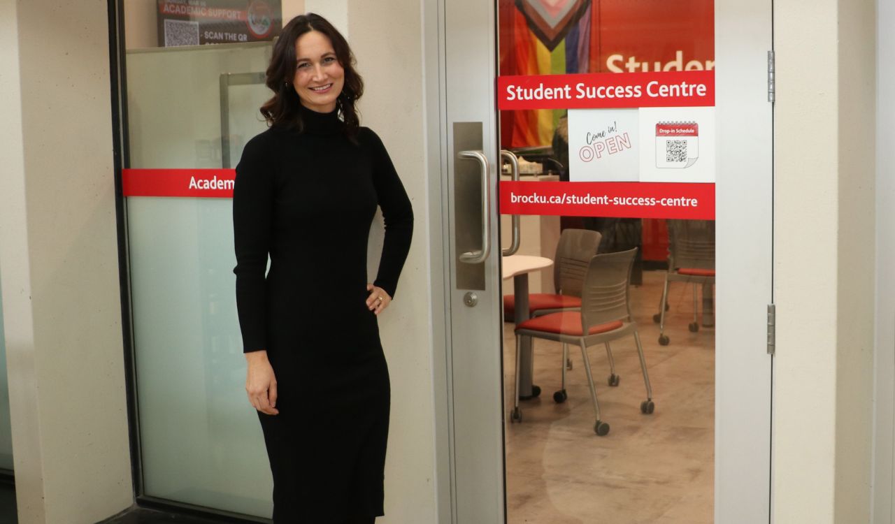 A woman stands in front of an indoor glass doorway that says'Student Success Centre.'