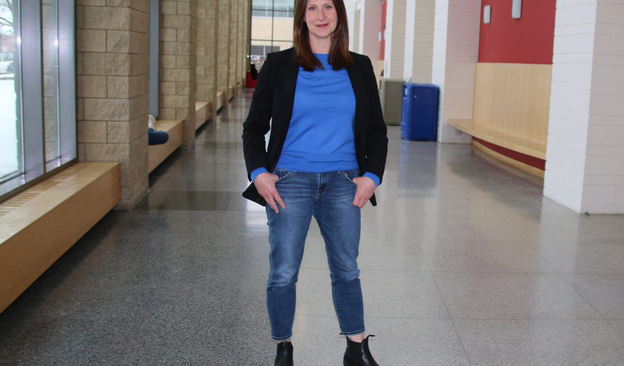 A woman in a blue shirt stands in an indoor hallway.