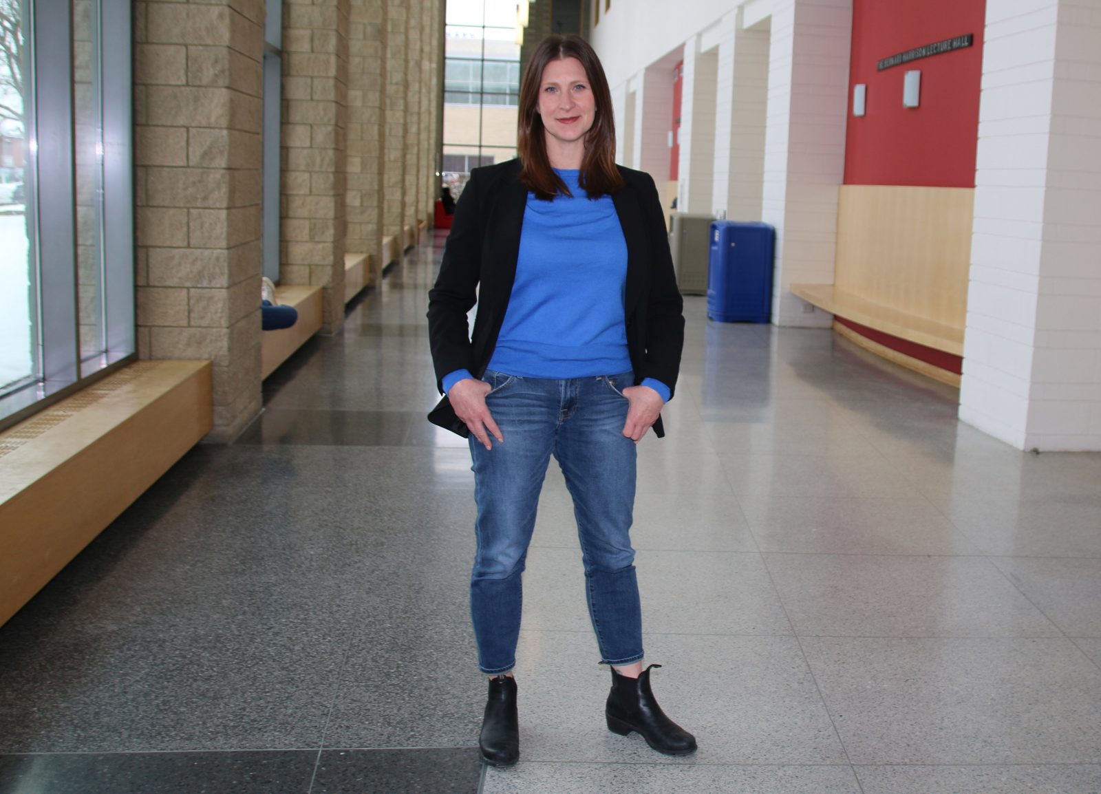 A woman in a blue shirt stands in an indoor hallway.
