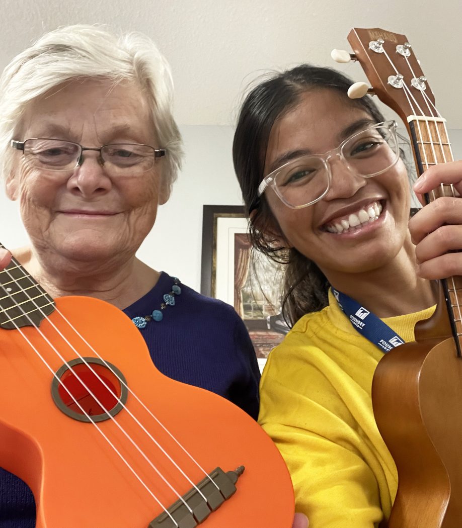 An elderly woman and younger woman smile while holding ukuleles.
