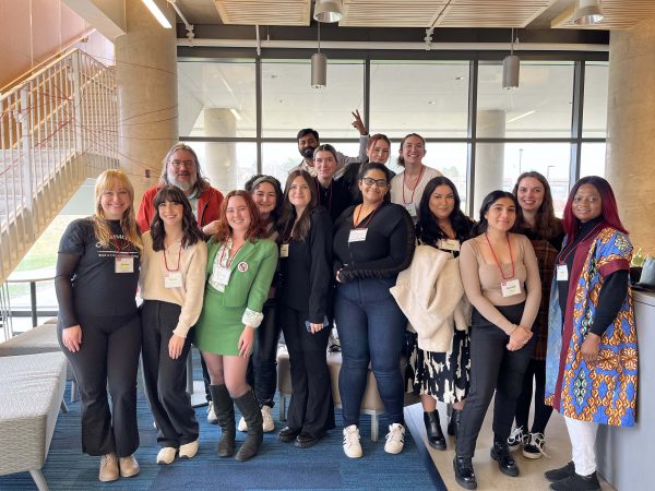 A group of fourteen students and their professor, all wearing nametags, pose near a window at the Marilyn I. Walker School of Fine and Performing Arts