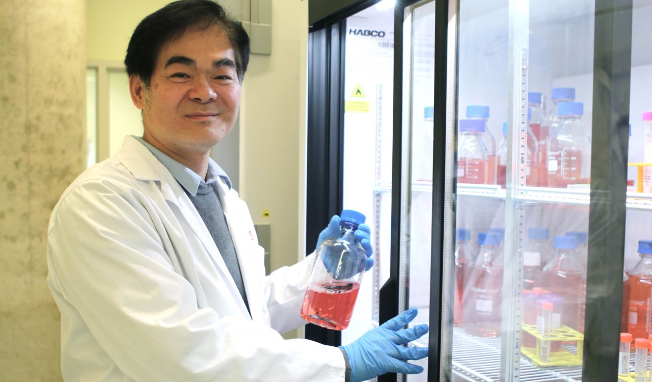 Newman Sze smiles into the camera as he stands next to a refrigerator in his lab.