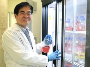Newman Sze smiles into the camera as he stands next to a refrigerator in his lab.