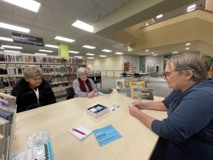 Three elderly people sit around a table playing trivia at the public library.