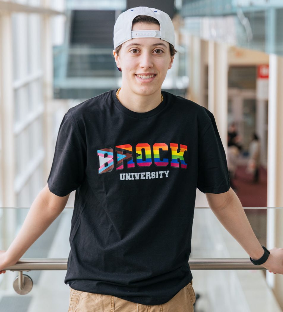 A student wears a black t-shirt with a rainbow-coloured Brock logo on it.