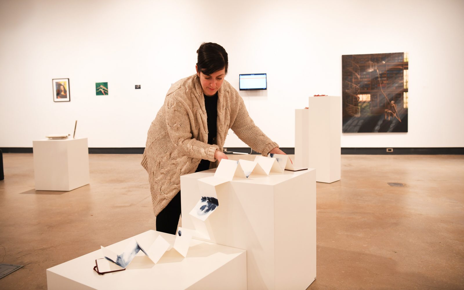 A female curator gently placing a long piece of paper that has been unfolded from a book in a gallery space.
