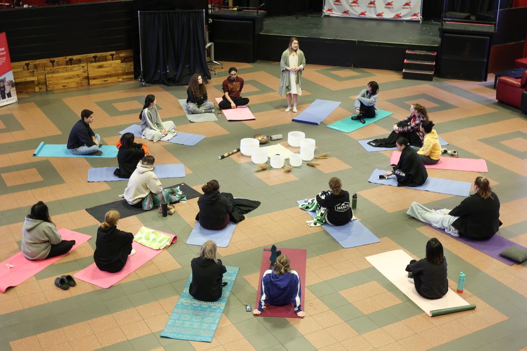 People sit on the floor on yoga mats in a semi-circle.