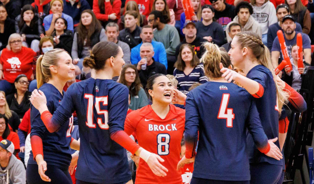 A team of women’s volleyball players celebrate a point in front of a crowd.