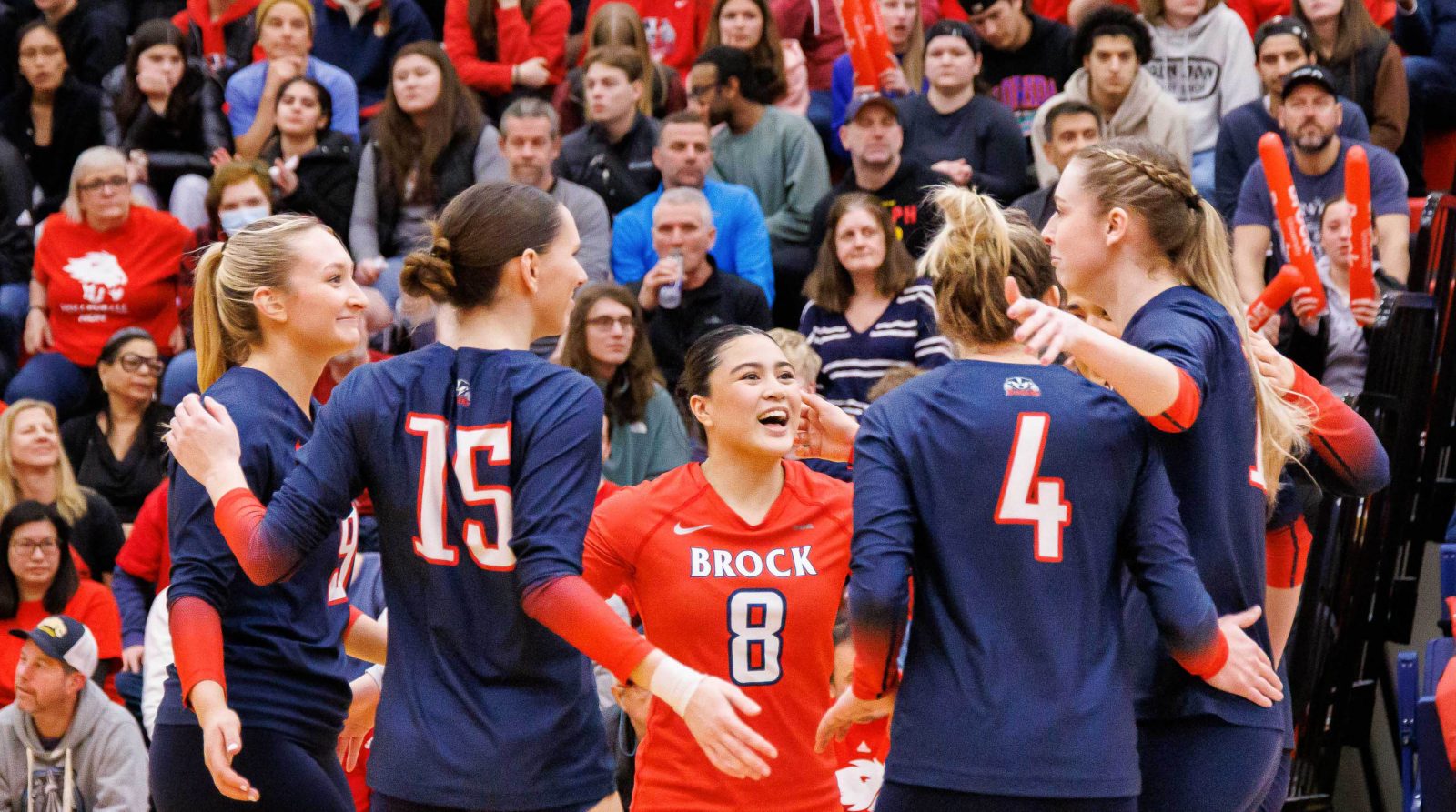 A team of women’s volleyball players celebrate a point in front of a crowd.