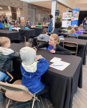 A woman speaks to two children at a table in a mall.