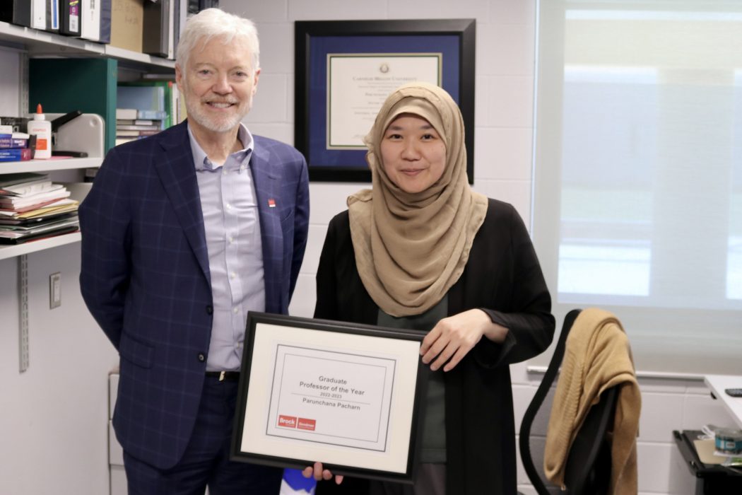 Two people hold a frame with the teaching award in an office.