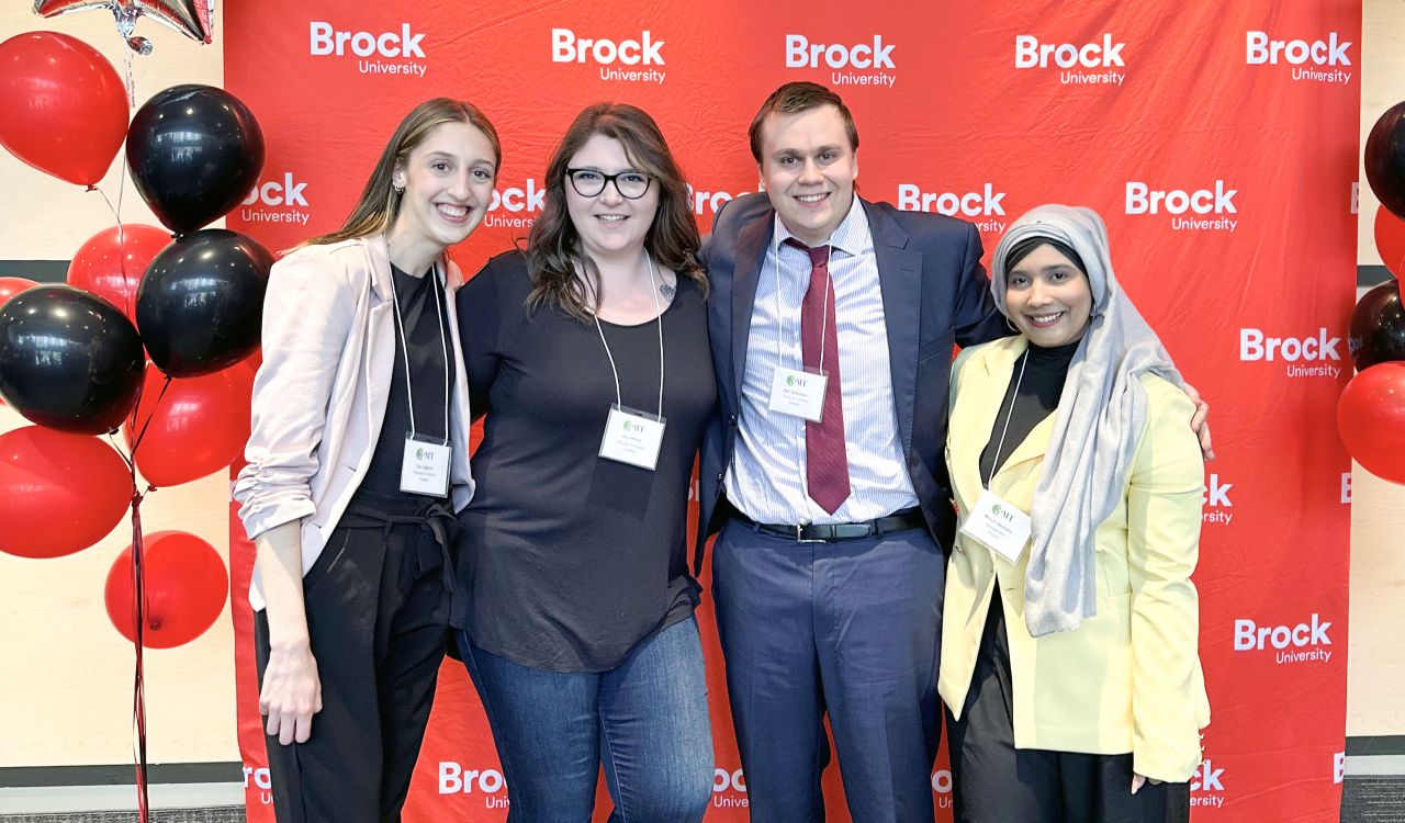 Four people beside each other in front of a Brock branded backdrop.