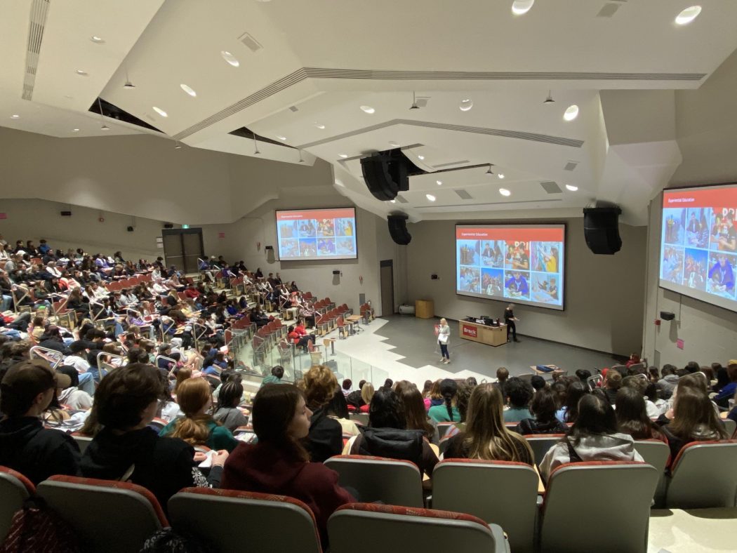 High school students sit in a large lecture hall listening to a presentation.